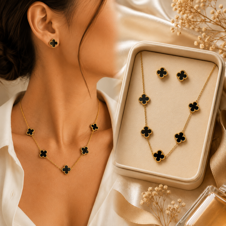 Imagem elegante de uma mulher usando conjunto de colar e brincos dourados com detalhes em formato de trevo preto, ao lado de uma caixa de joias exibindo o mesmo conjunto sobre tecido acetinado em tons claros.